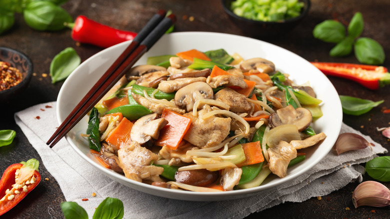 Chop suey in white bowl surrounded by ingredients