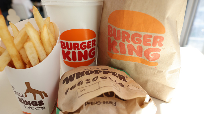 A Whopper meal from Burger King with fries and a drink and then a Burger King bag to one side