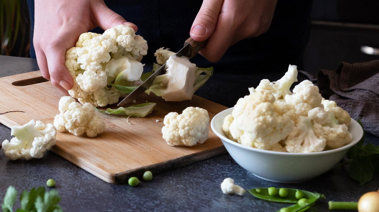 Closeup of person chopping cauliflower with a chef's knife