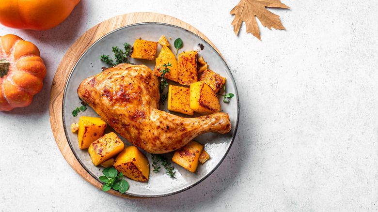 An autumn theme photo of a roast chicken thigh along with roasted squash on a nice plate