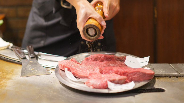hands grinding pepper onto raw steaks