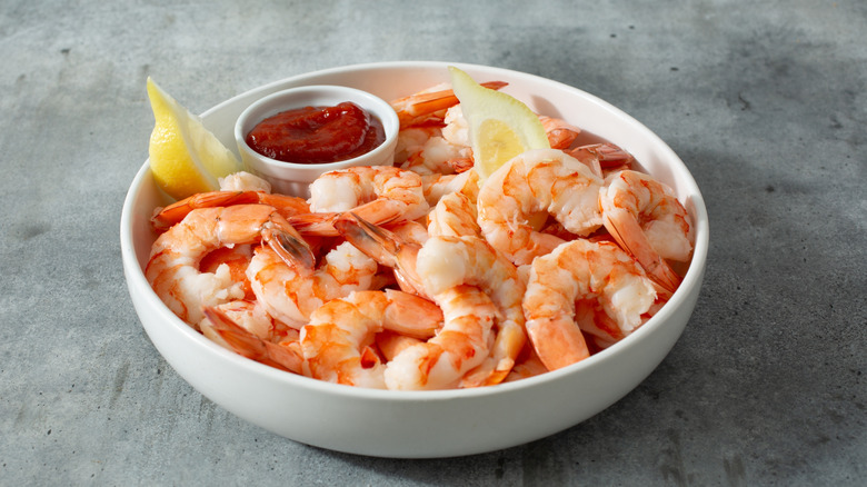 Shrimp cocktail in white bowl with cocktail sauce and lemon slices