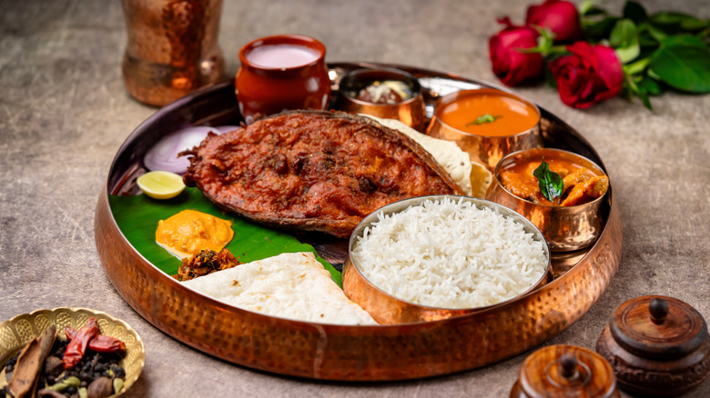 Copper plate laden with rice, fish, flatbread, and various curries