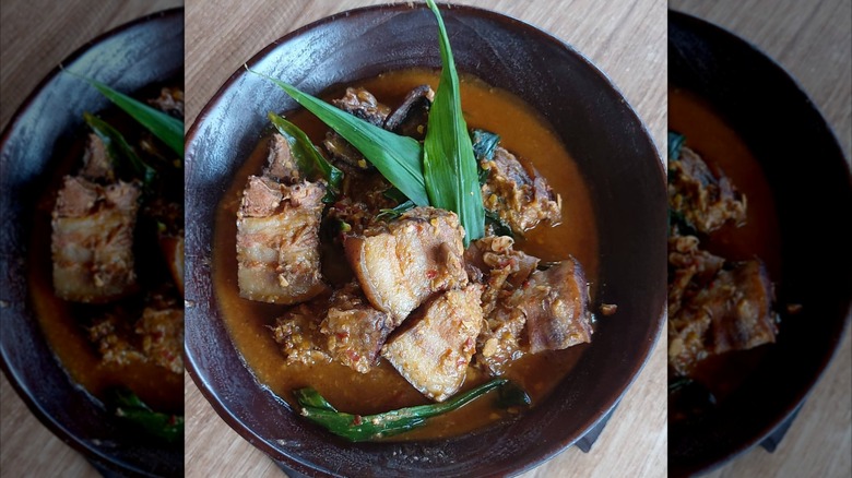 Bowl full of smoked pork with axone, topped with green leaf garnishes