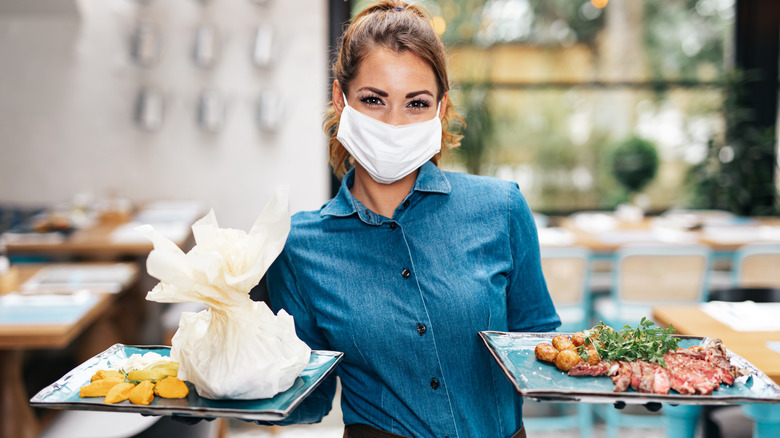 A waitress carrying plates, wearing a face mask