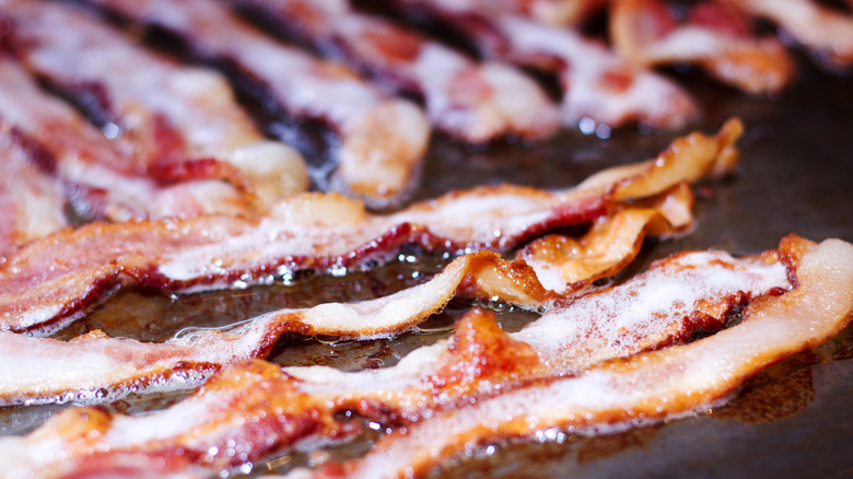 Strips of bacon frying in grease on a flat-top grill