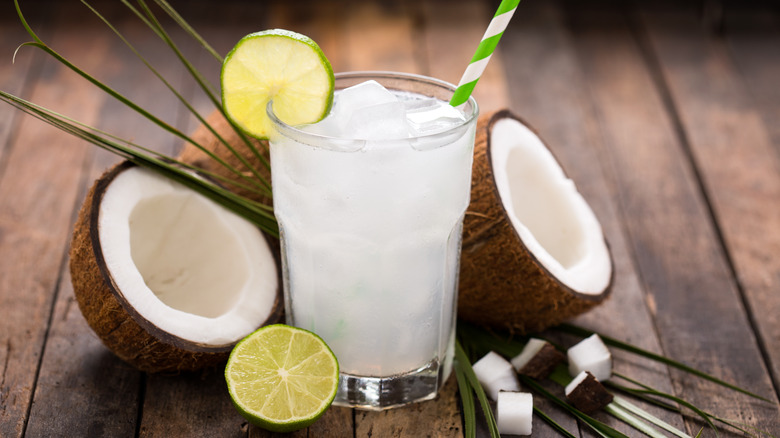 A glass of coconut water and coconuts sliced in half