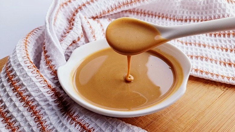 Peanut sauce with spoon in a bowl with a kitchen towel behind it