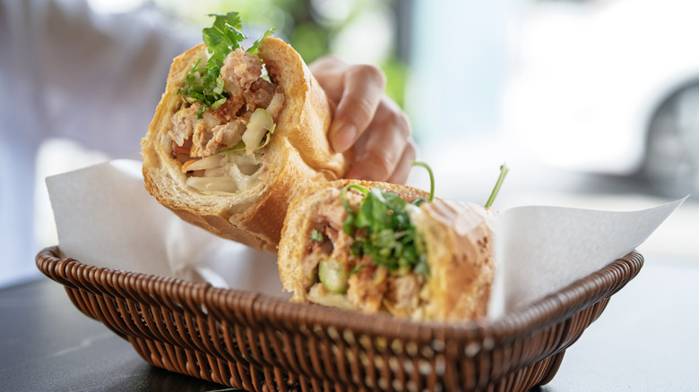 Hands holding a banh mi sandwich with pickled vegetables
