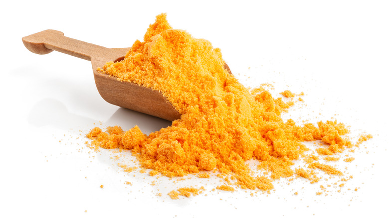 Wooden serving scoop full of bright yellow cheese powder on a white background