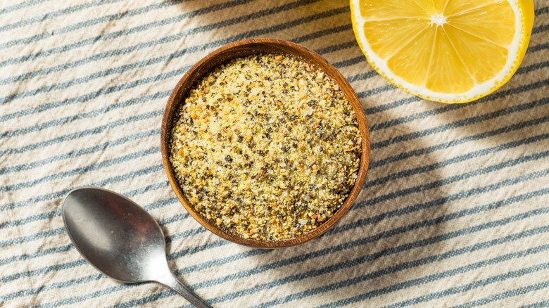 Bowl of lemon pepper seasoning next to a spoon and halved lemon