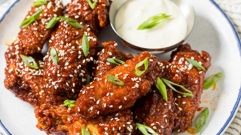 Plate of Korean fried chicken wings topped with scallions next to a dip