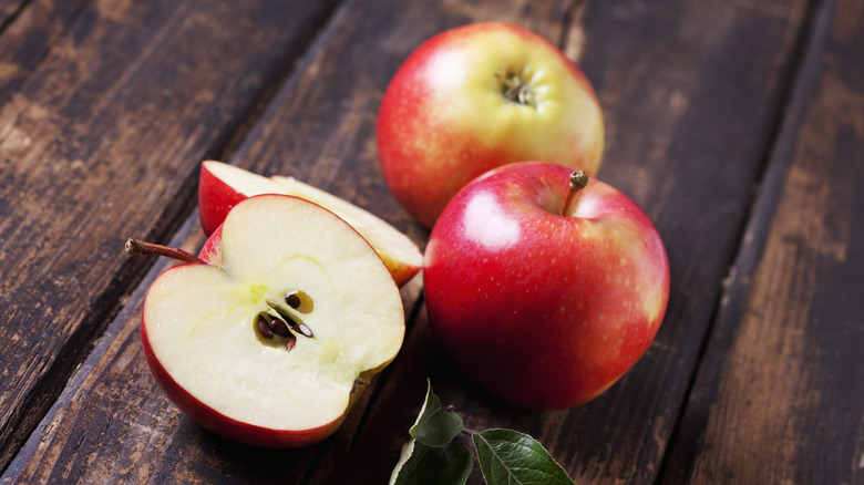 Whole and sliced apples on wooden surface