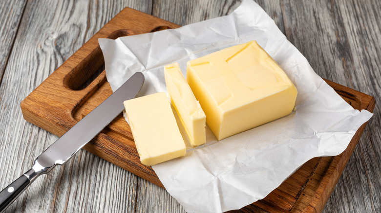 Sliced block of butter on wooden cutting board with knife