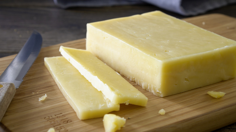 Sliced block of cheddar cheese on wooden cutting board