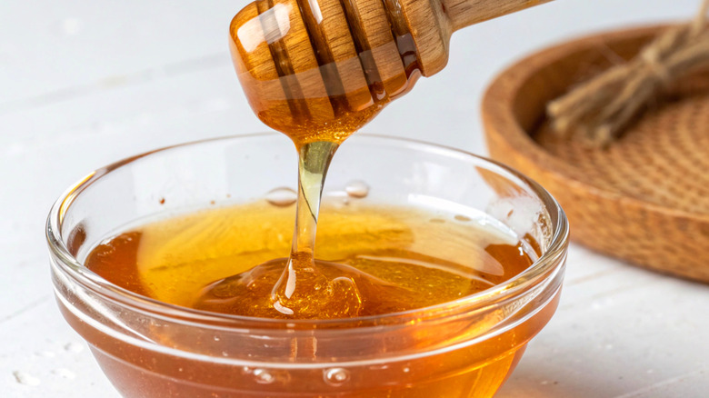 Honey drizzling from wooden dipper into bowl