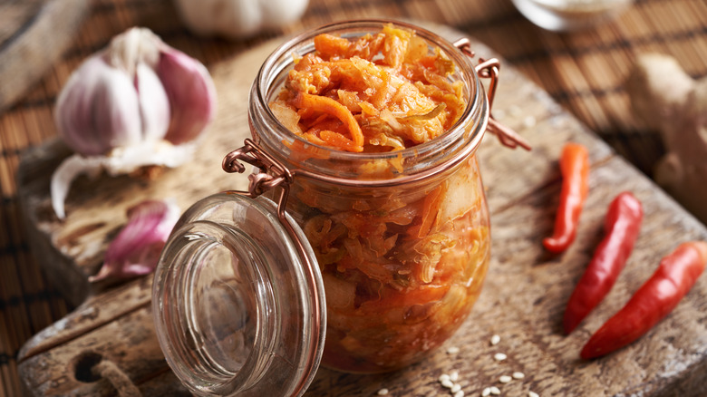 Jar of kimchi of wooden cutting board with garlic bulb and red chile peppers