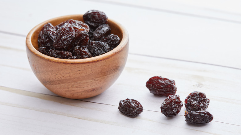 Dried raisins in wooden bowl with some spilling out