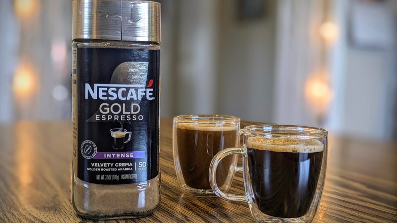 NesCafe Gold instant espresso jar and two espresso cups on wood table