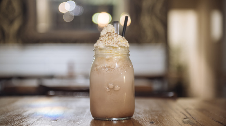 A jar of shaken coffee with whipped cream and a straw