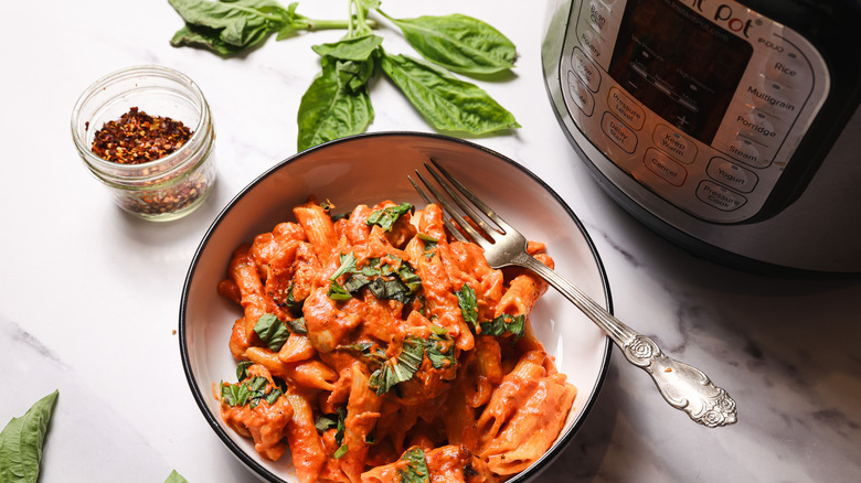 Penne pasta in creamy tomato sauce in bowl with Instant Pot besides it