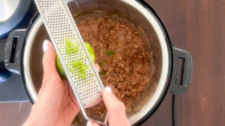 hands zesting lime into pot with refried beans