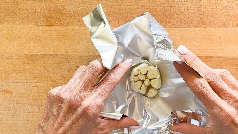 hands wrapping garlic bulb in foil