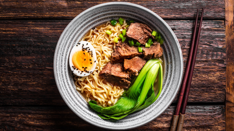 A bowl of ramen with beef, pak choi, egg, salad onions