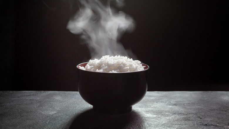 A steaming bowl of rice in a dark room on top of a table surface