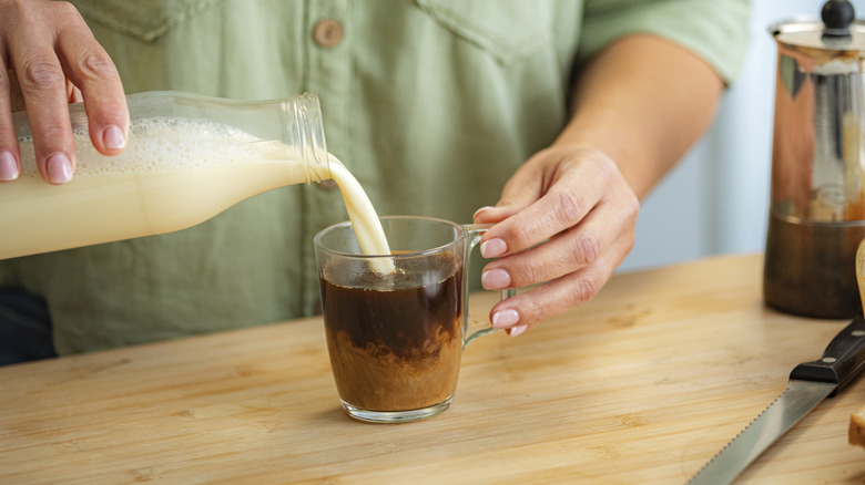 A person pouring creamer into a cup of coffee