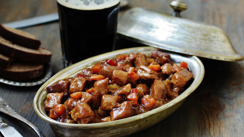 A bowl of Guinness Irish stew next to a poured pint and a plate of brown bread