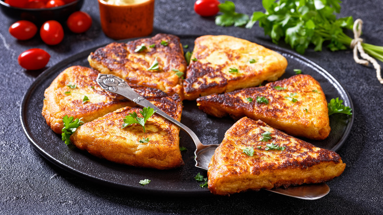 Six slices of Irish potato farl arranged on a black plate, resting on a black wooden surface, with one slice topped with butter being lifted by a silver cake server