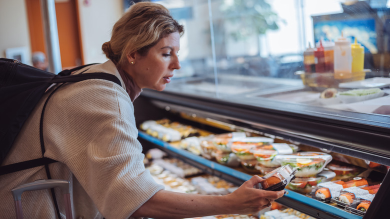 A woman looking at a pre-packed sushi tray in a convenience store