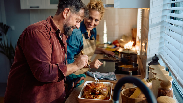 A couple smiling and cooking Thanksgiving turkey