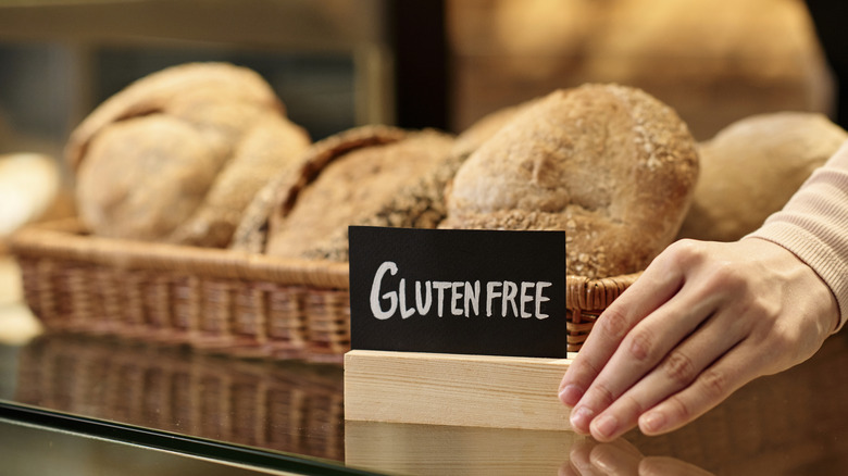 A person putting a "gluten free" sign in front of a basket of bread