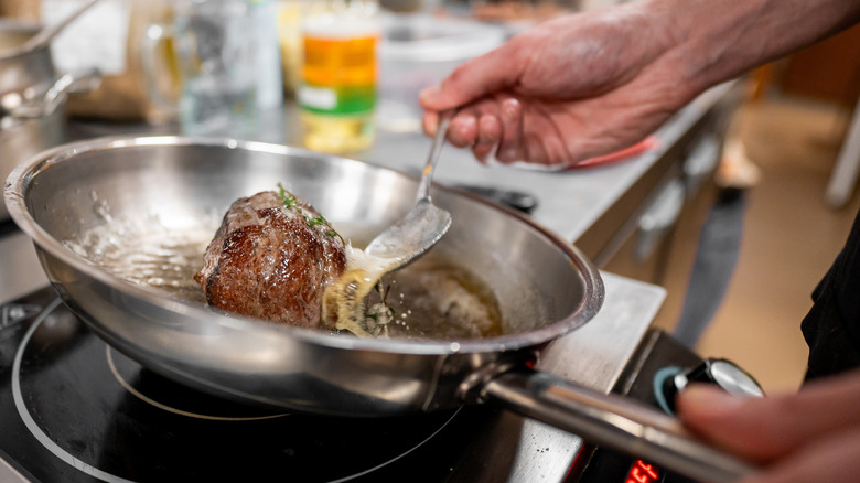 A man searing and basting a steak in a stainless steel pan