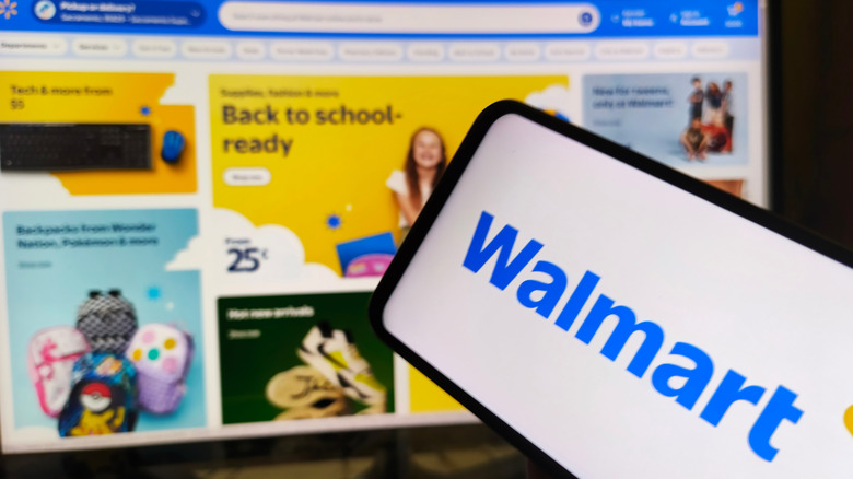 Mobile phone displaying Walmart logo in front of computer screen displaying front page of Walmart's website