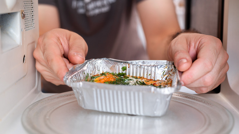 A person placing a metal dish of food into a microwave oven