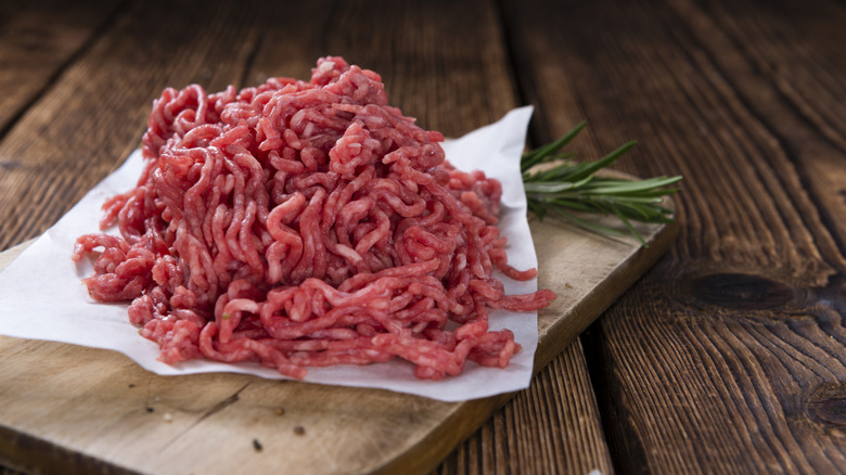 Raw ground beef on a square of parchment paper a top of wooden cutting board