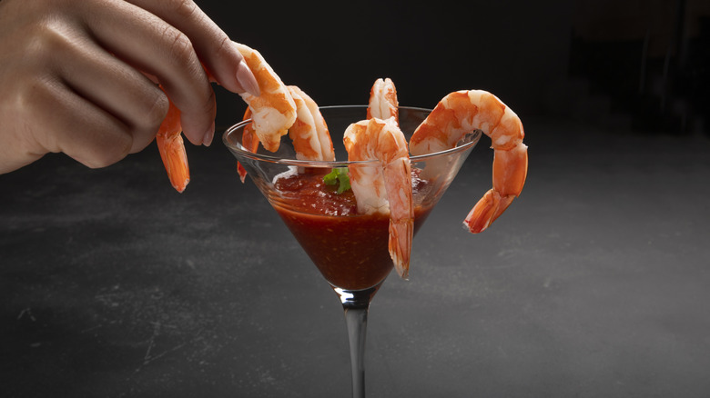 A person picks a shrimp out of a shrimp cocktail in a martini glass