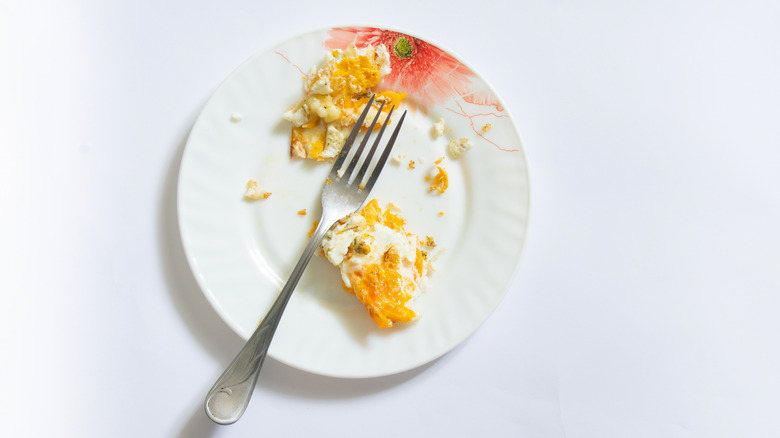 Leftover eggs on a white plate with a fork on a white backgroudn