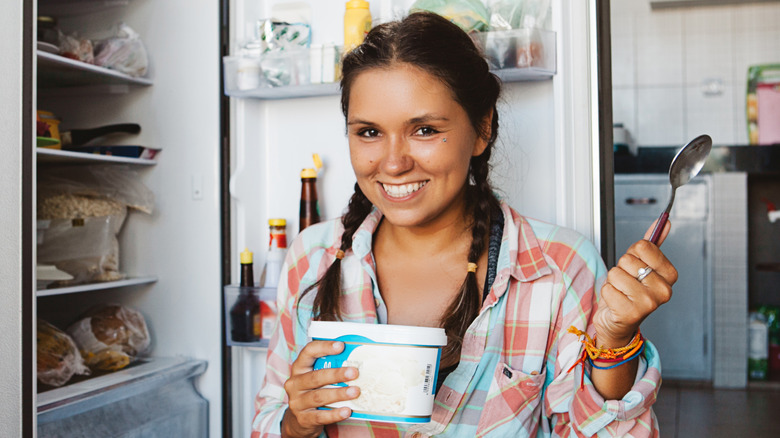 young woman eating ice cream in front of fridge