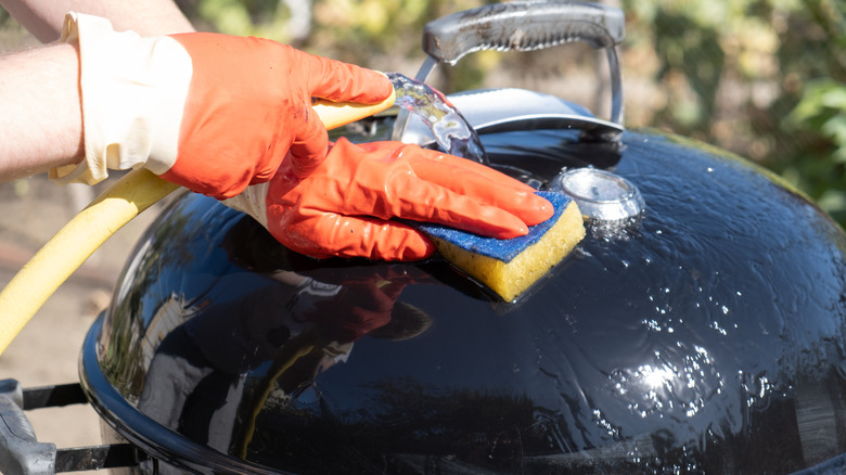 Cleaning the top of a grill with a garden hose and a sponge