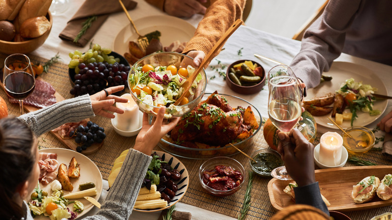 People pass dishes and cheers wine glasses over a feast table