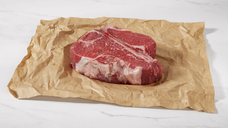 Sheet of brown butcher paper spread out on white marbled surface with raw beef steak on top