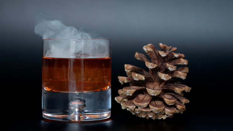 Smokey bourbon cocktail next to a pine cone