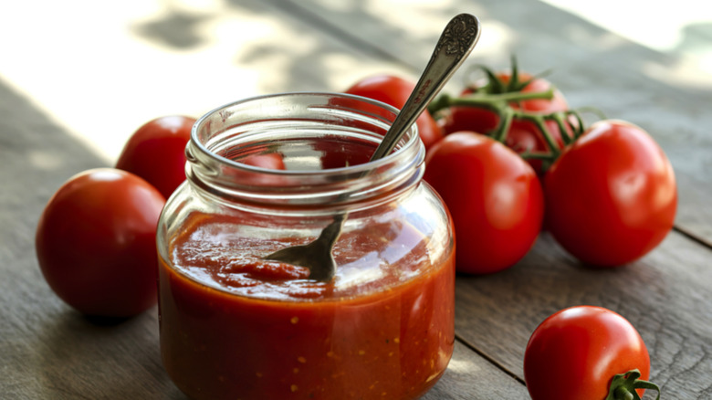 Mason jar filled with red sauce surrounded by ripe tomatoes