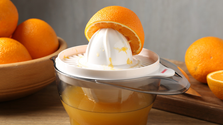 A halved orange on a countertop orange juice reamer filled with juice