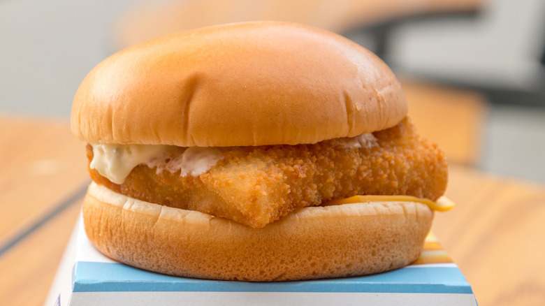 a McDonald's Filet-O-Fish sandwich sitting atop its cardboard box on a wooden table
