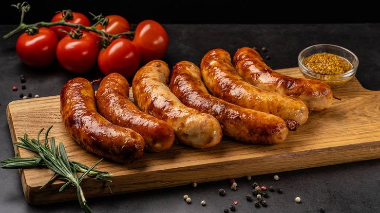cooked sausages on cutting board with mustard and fresh tomatoes